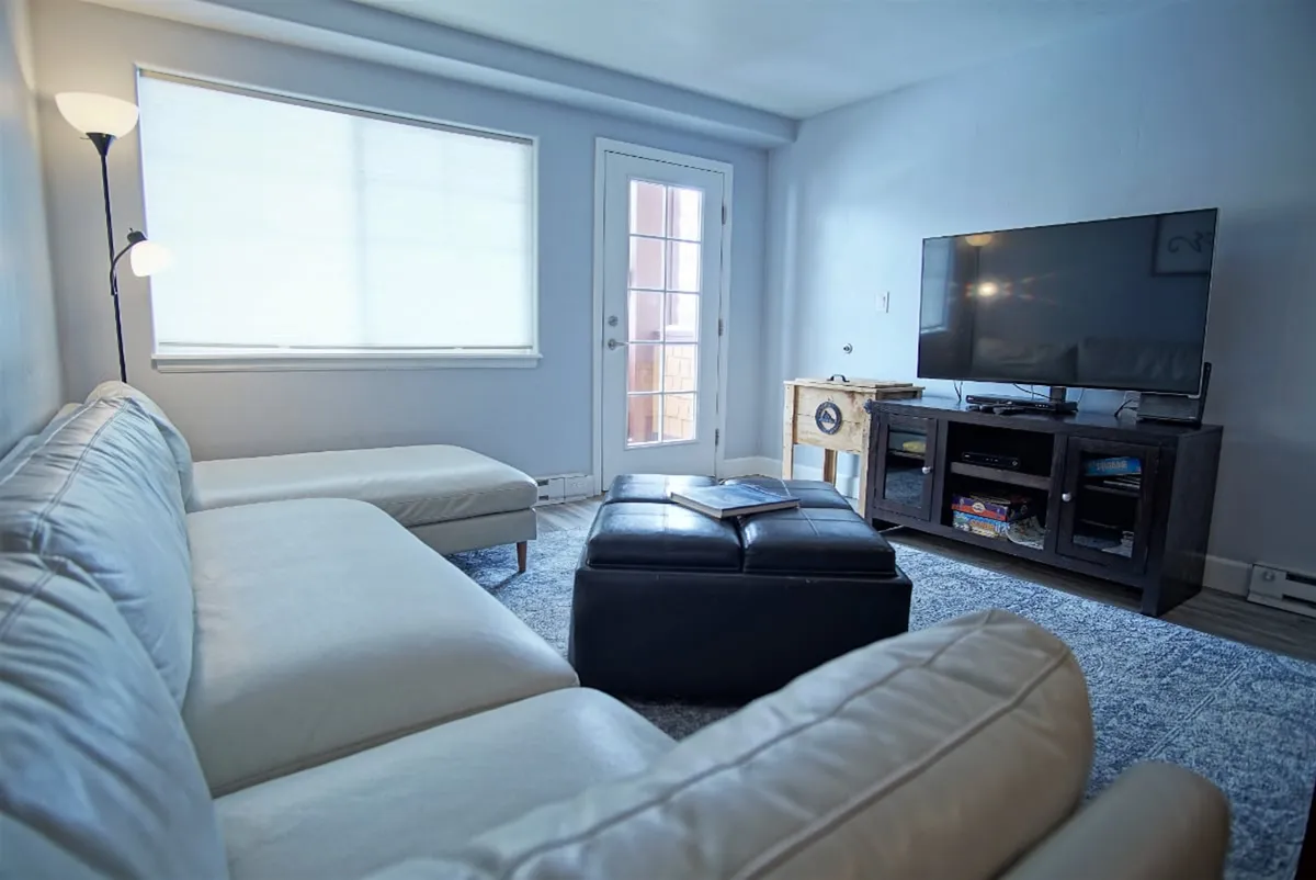 This image features a comfortable sofa and ottoman positioned around a television, with a window and door suggesting a connection to the outdoors. The space is arranged for socializing, relaxing, watching TV, or unwinding after a day of adventure.