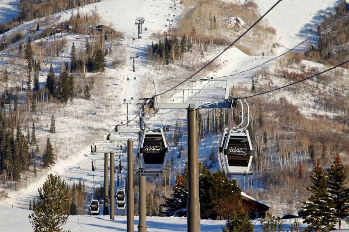 This image captures the gondola lift gliding over snow-covered slopes, surrounded by tall pine trees with a stunning mountain backdrop. The gondola is the focal point, visually connecting the property to ski access and outdoor adventure.