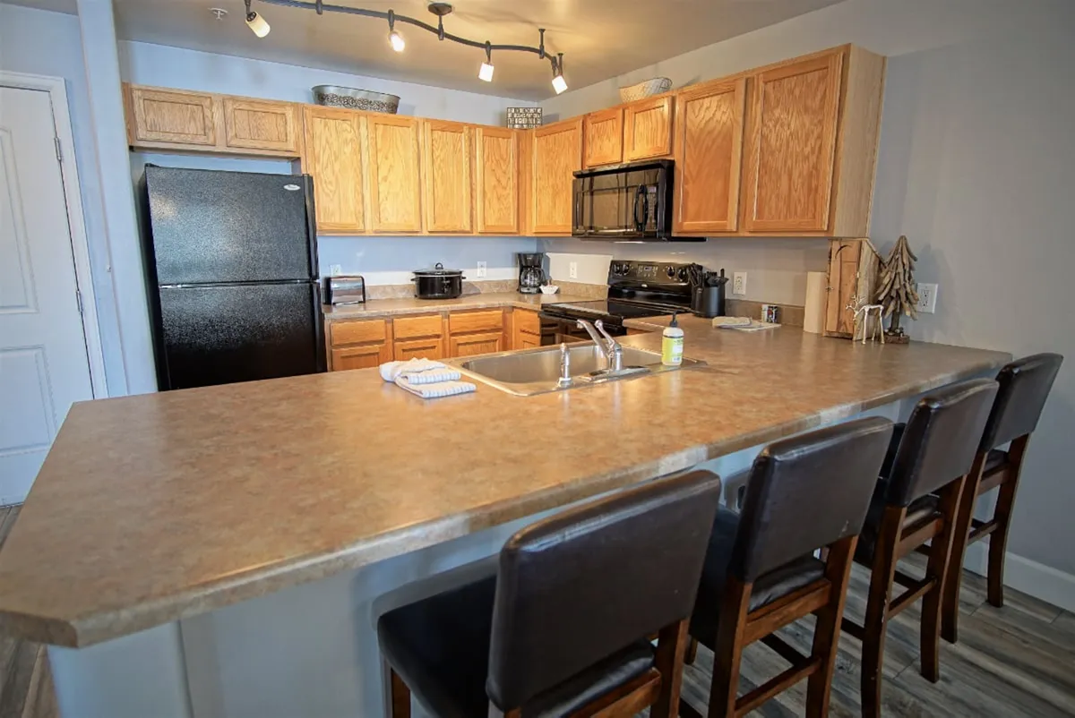 A warm and welcoming modern kitchen with a countertop and bar stools, surrounded by wooden cabinetry and modern appliances. The setup invites gatherings and shared moments, ideal for relaxing after exploring or working remotely.