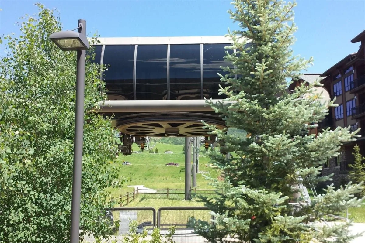 An exterior shot of the cable car (gondola) station amid green surroundings, with mountains rising in the backdrop. The scene suggests access to both winter sports and summer mountain adventures.