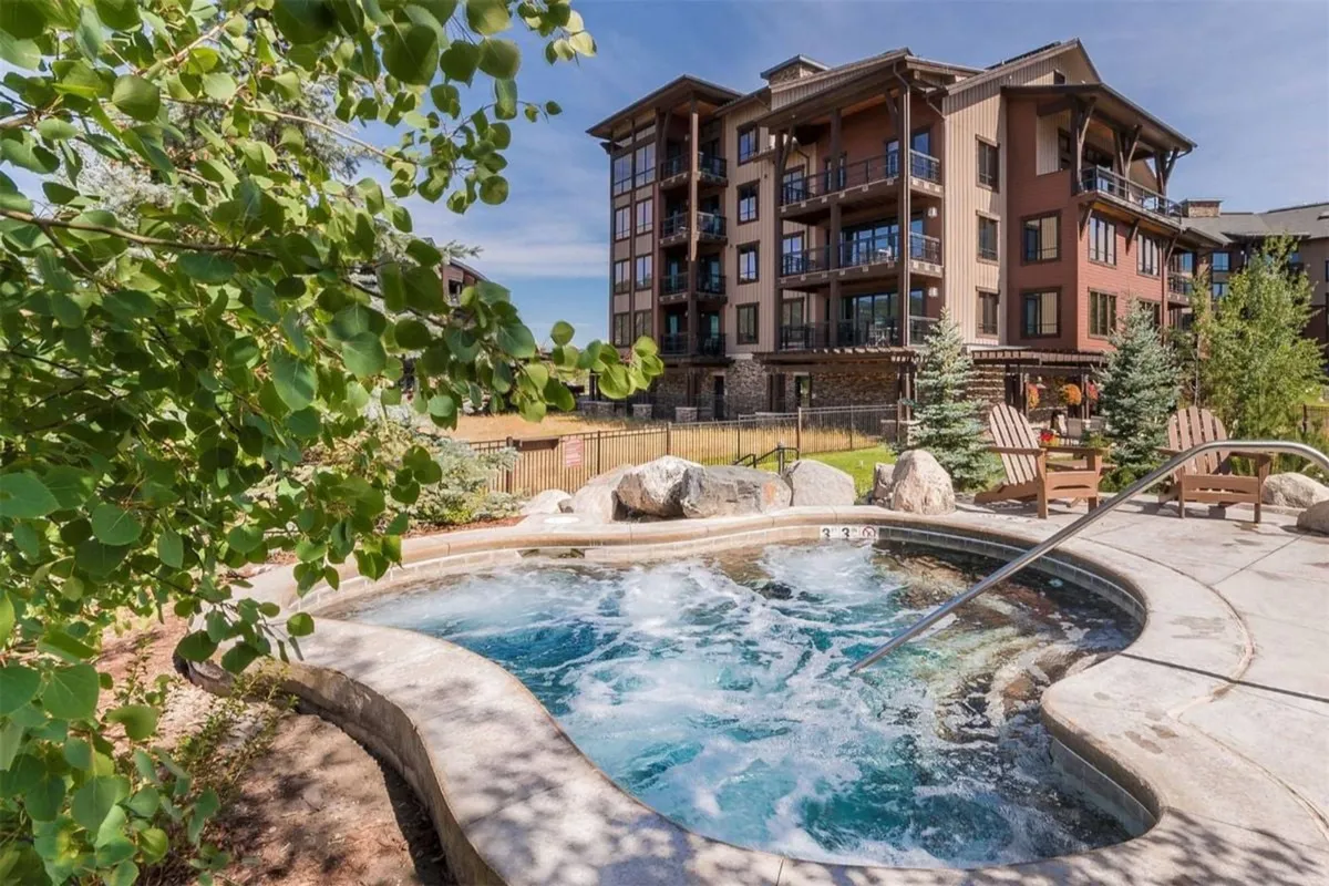 An inviting hot tub encircled by lush greenery and set against the apartment building, with people relaxing and socializing in the tranquil outdoor setting. The evening lighting hints at sunset views and the possibility of stargazing.