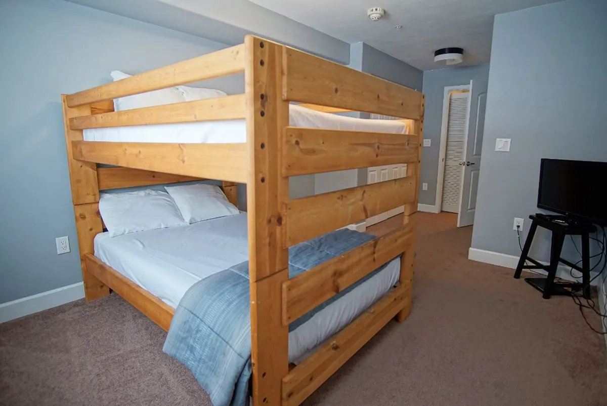 A cozy second bedroom designed for versatility, featuring a full-over-full bunk bed with a twin bed, as well as a television and plush carpet. The setup is ideal for families or groups, offering both sleep space and entertainment.