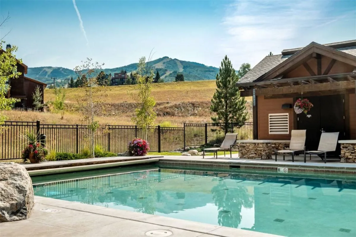 The exterior features a sparkling heated swimming pool surrounded by comfortable lounge chairs and vibrant flower beds, all set against the breathtaking backdrop of Steamboat Springs’ majestic mountains. The scene evokes relaxation and social enjoyment, ideal for swimming, sunbathing, or gathering with friends and family.