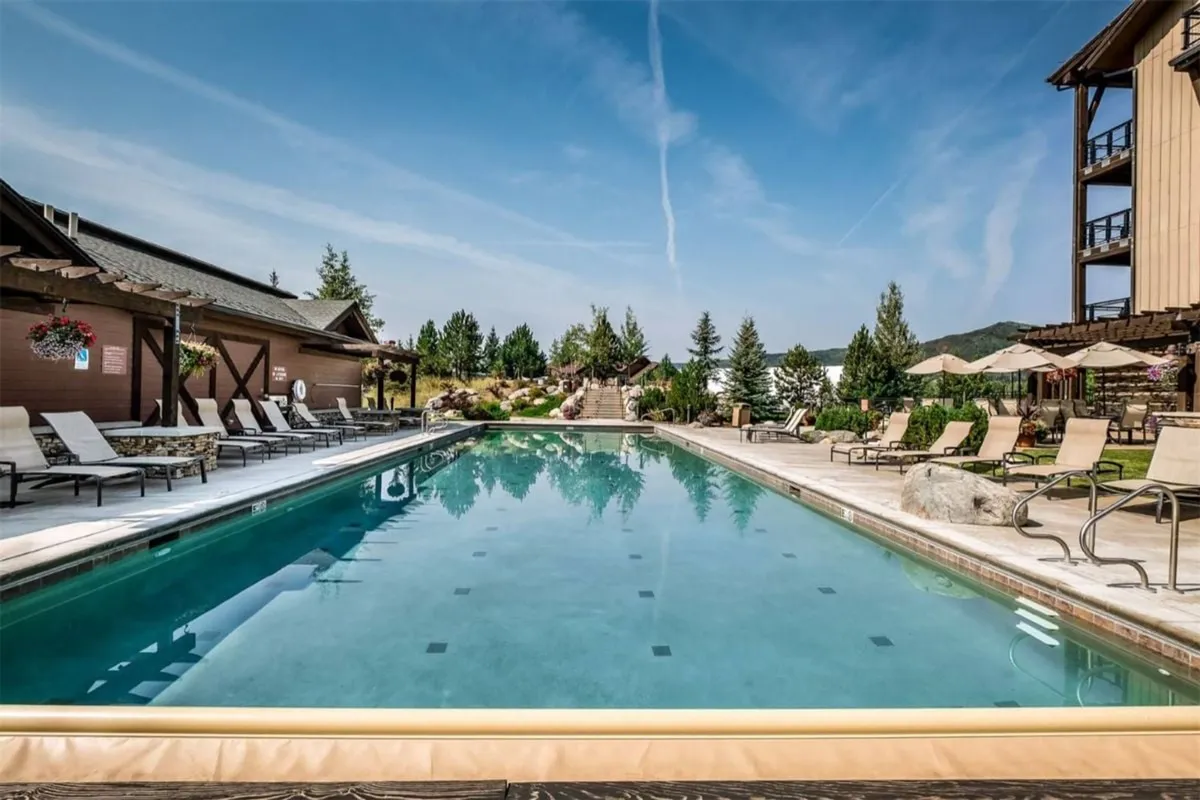 A sun-drenched swimming pool surrounded by lounge chairs and manicured gardens, with the building’s facade in the background. The scene suggests a leisurely, resort-style atmosphere perfect for swimming, sunbathing, or relaxing with friends.